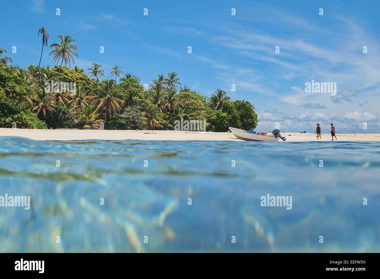 Unberührte karibische Insel mit tropischer Vegetation und ein Boot am Strand mit Touristen, gesehen von der Meeresoberfläche, Panama Stockfoto