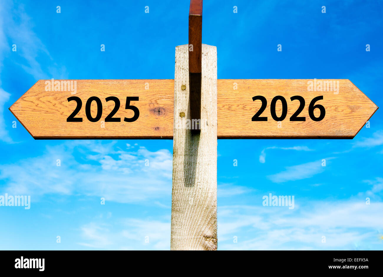 Wegweiser aus Holz mit zwei entgegengesetzte Pfeile über klaren, blauen Himmel, Jahr 2025 und 2026 Zeichen, Happy New Year Konzeptbild Stockfoto
