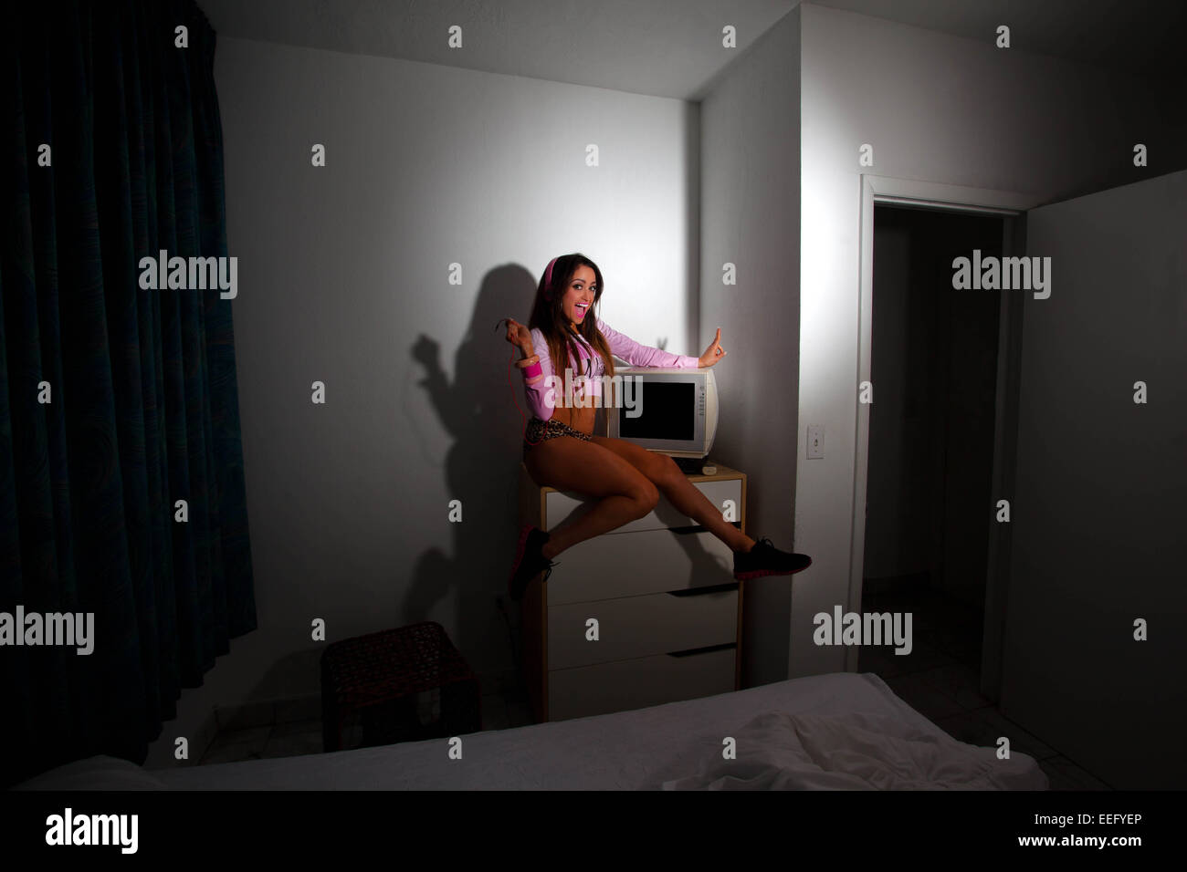 Junge hübsche Latino Frau sitzt in einem Hotelzimmer einen Vintage Fernseher über den Kopf heben Stockfoto