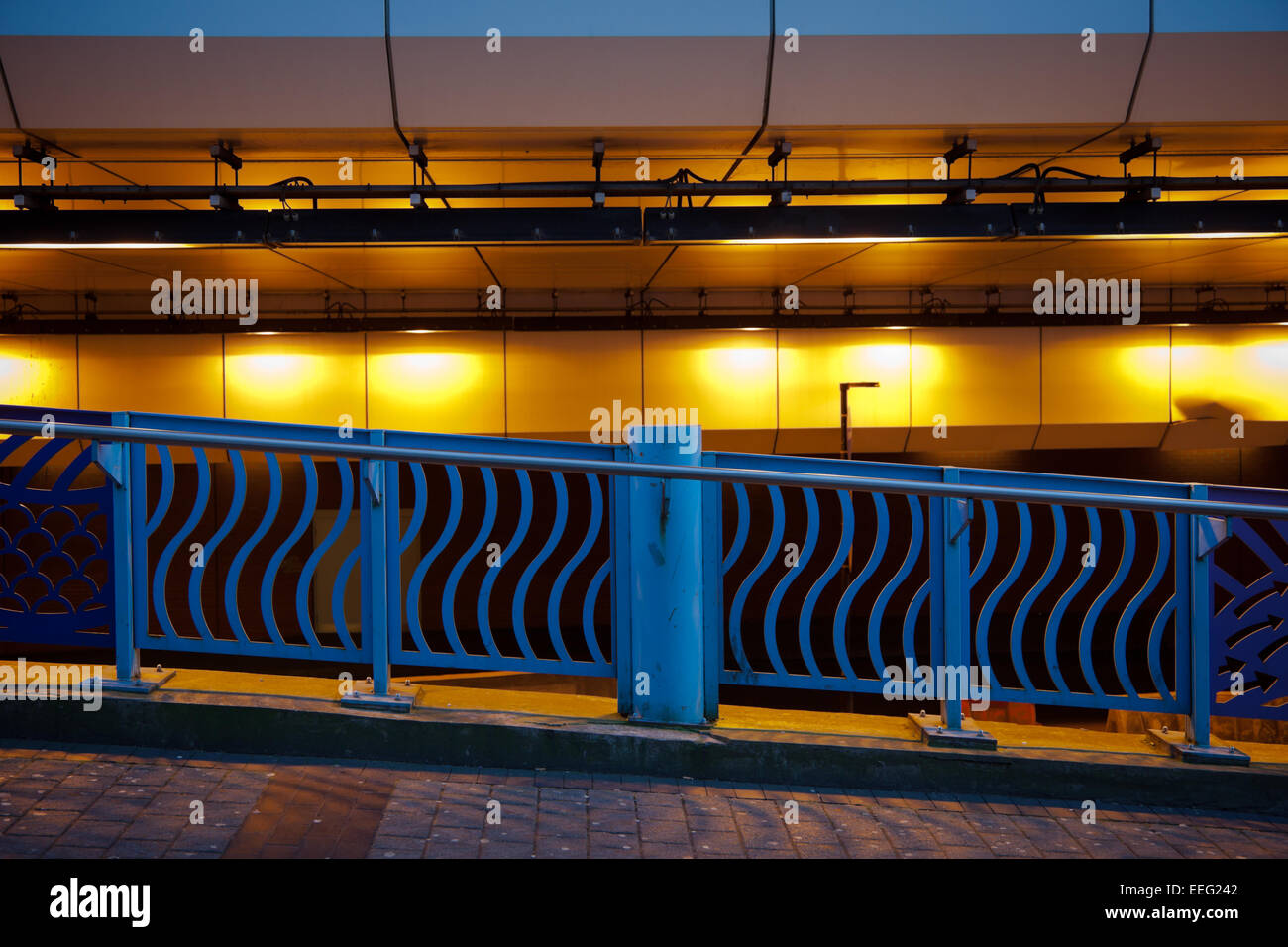 Gehweg beleuchtet durch Natrium-Lampen mit seinen gelben Schein und eine blau lackierten Schiene, Birmingham UK Stockfoto