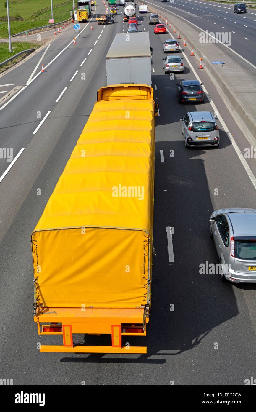 Luftaufnahme von oben Gelber lkw-Sattelzug & Anhänger langsam fahrender Autobahnstau mit zwei Fahrspuren Hindernisse voraus Essex England UK Stockfoto