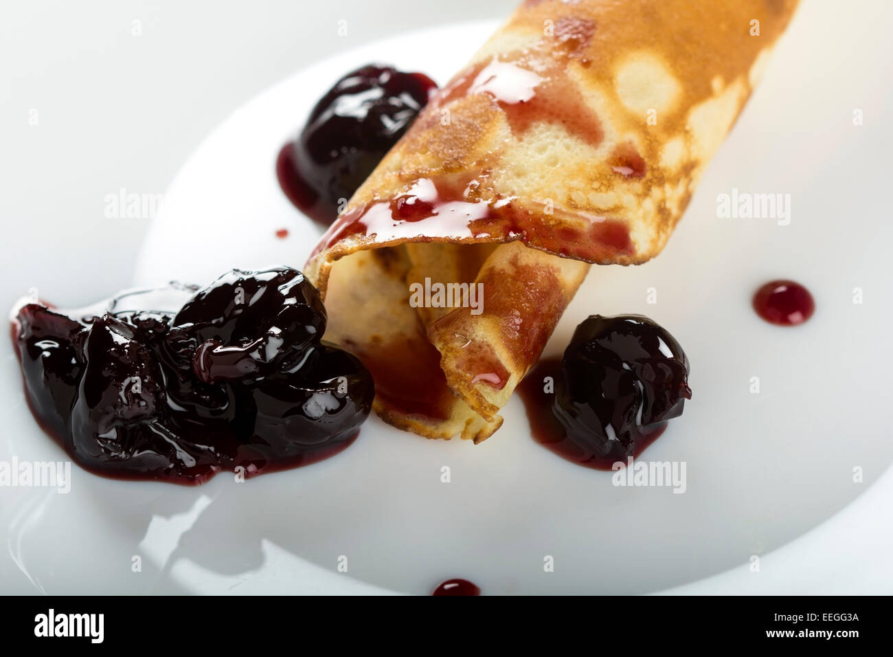Nahaufnahme von einem Pfannkuchen mit schwarzen Kirschen Marmelade auf einem weißen Teller Stockfoto