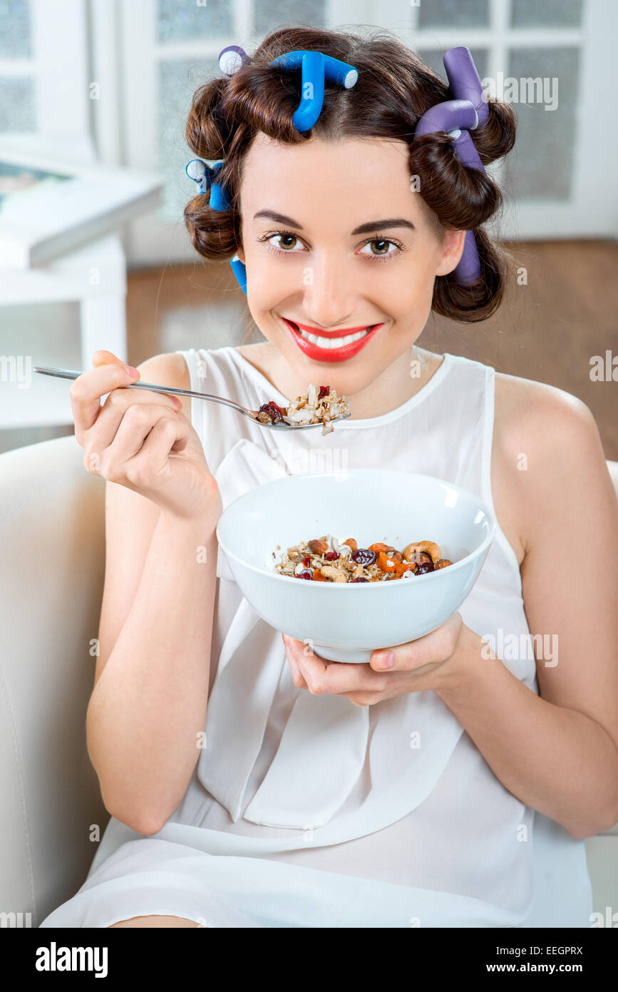 Junge Frau mit Lockenwickler Müsli frühstücken sitzen auf der Couch zu Hause Stockfoto