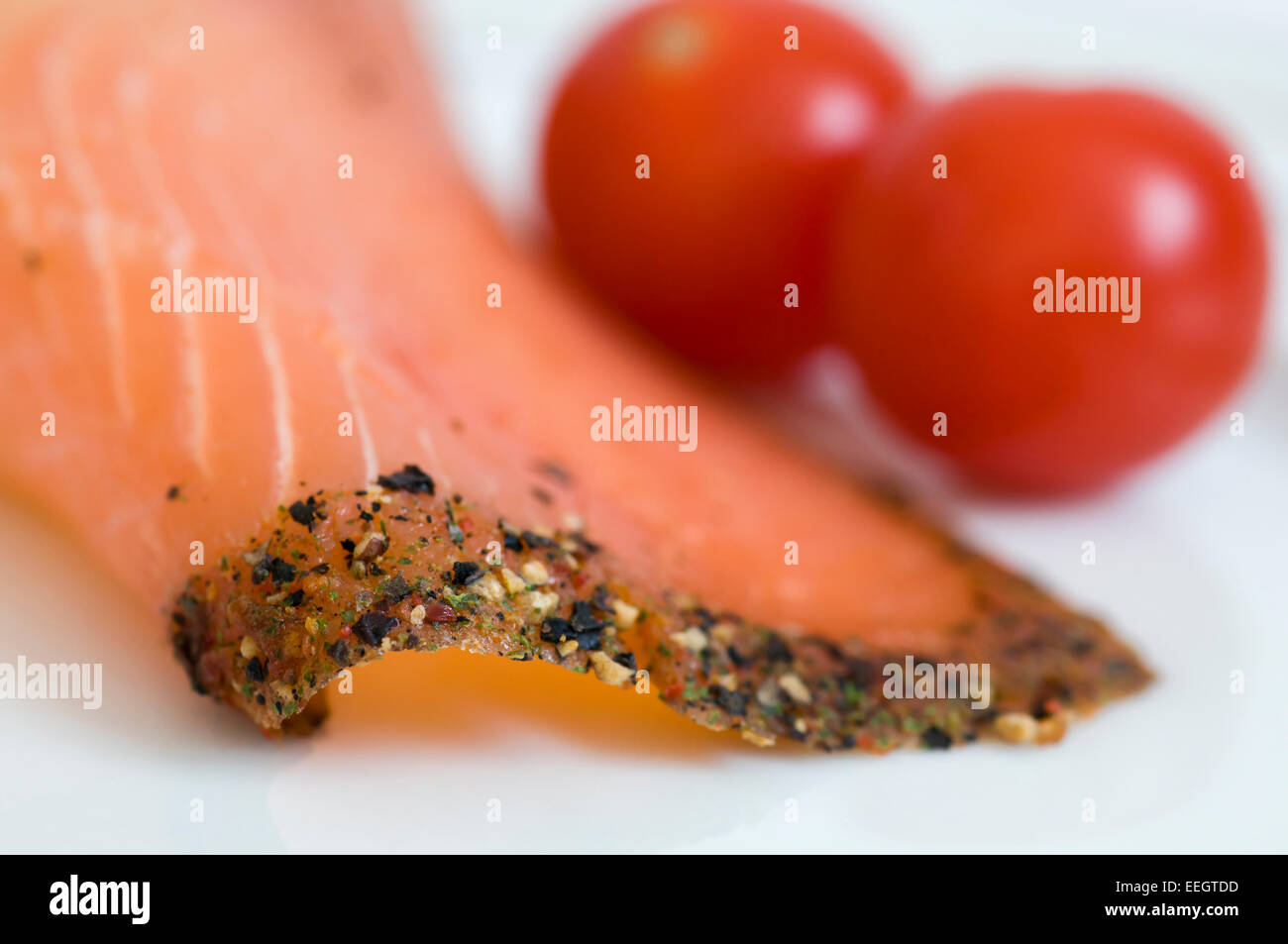 Nahaufnahme von geräuchertem Lachs Scheibe mit schwarzen Pfeffer-Rand und Tomaten im Hintergrund Stockfoto
