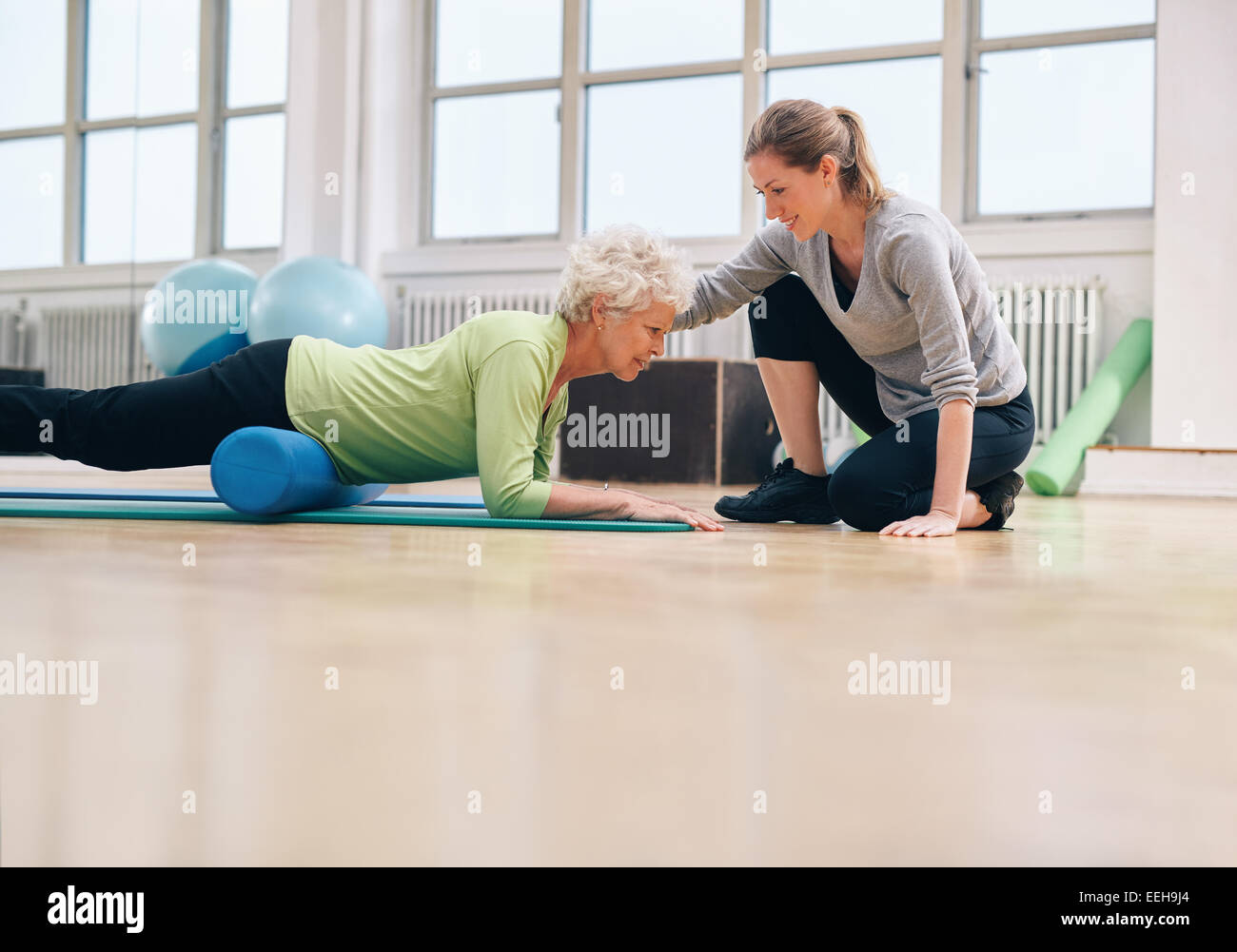 Ältere Frau mit einer Schaumrolle wird unterstützt durch personal Trainer im Fitness-Studio trainieren. Physiotherapeuten helfen senior Frau Stockfoto