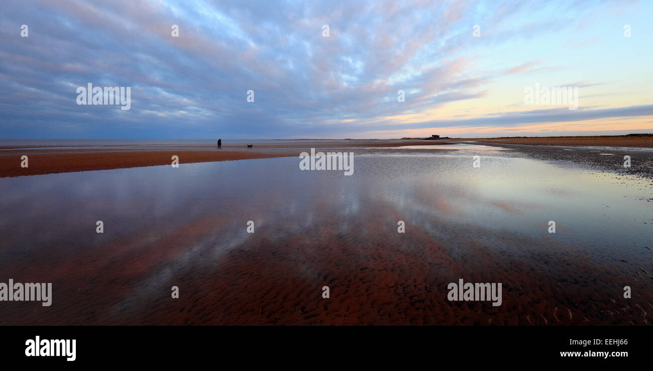 Frau und ihrem Hund zu Fuß nach Hause in der Abenddämmerung am Strand Brancaster in North Norfolk. Stockfoto