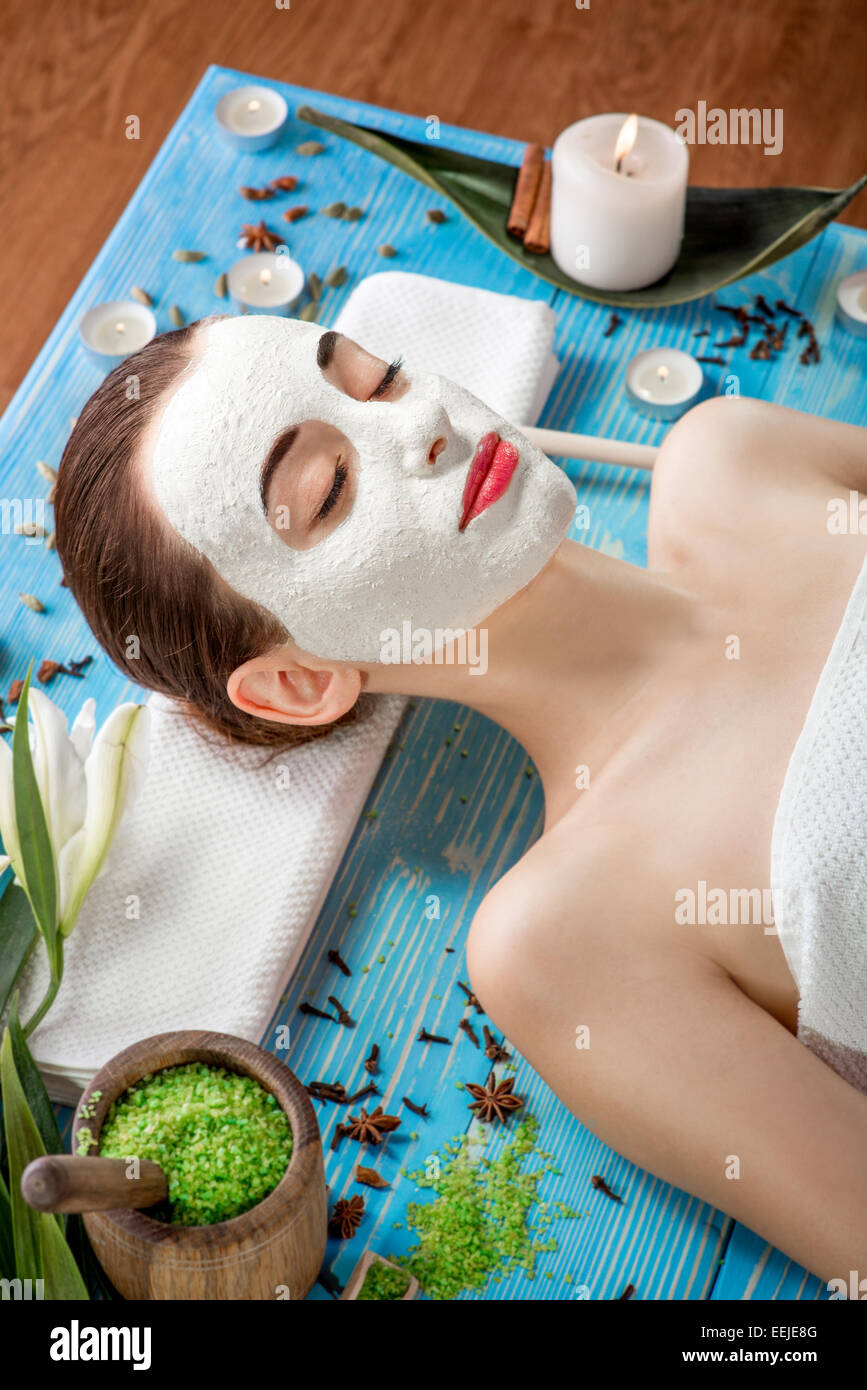 Junge Frau mit Spa Gesichts Maske auf ihr Gesicht auf blauer Tisch liegend mit Blumen, Kerzen und Meersalz im beaty salon Stockfoto