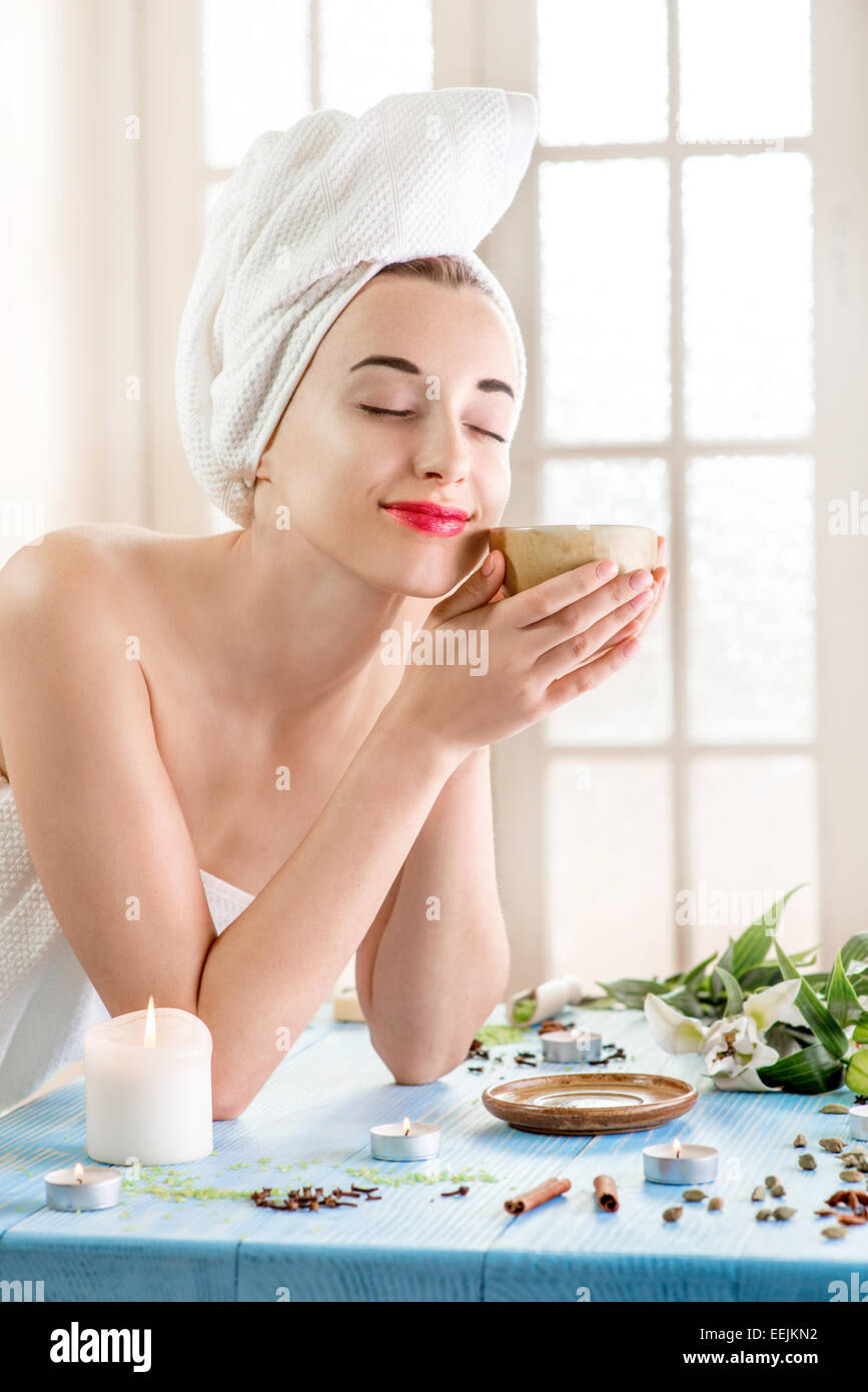 Lächelnde junge Frau mit Tasse Kräutertee in Badetuch im Wellness-Salon. Kräuterbehandlung. Stockfoto