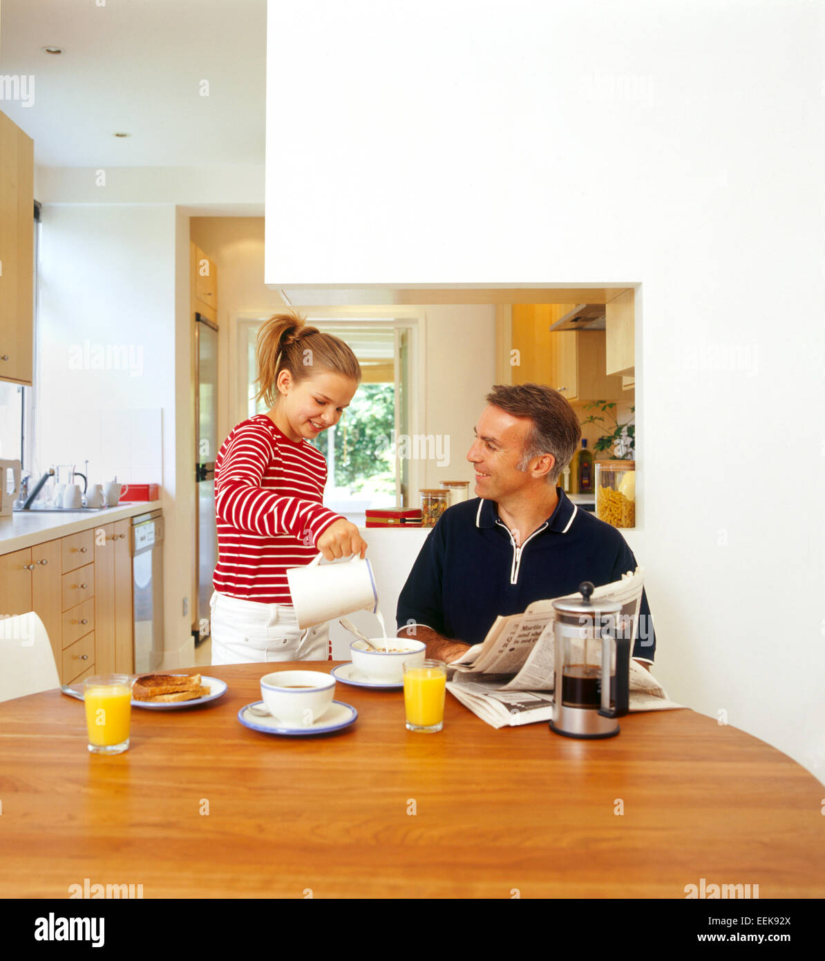 Vater und Tochter frühstücken zusammen, in Küche, Abbinden, lachen, während Tochter gießt Milch auf ihres Vaters Getreide Stockfoto