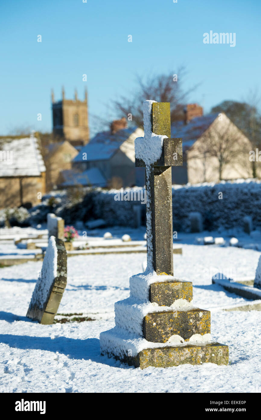 Grabstein Kreuz im Schnee auf einem Friedhof. Verstauen auf der Welt. Cotswolds, England Stockfoto