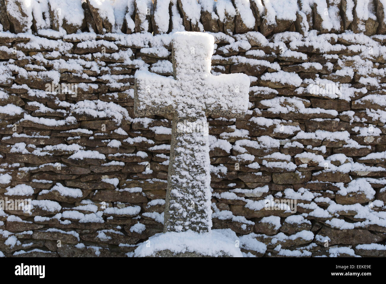 Grabstein Kreuz in den Schnee gegen eine Trockenmauer. Cotswolds, England Stockfoto