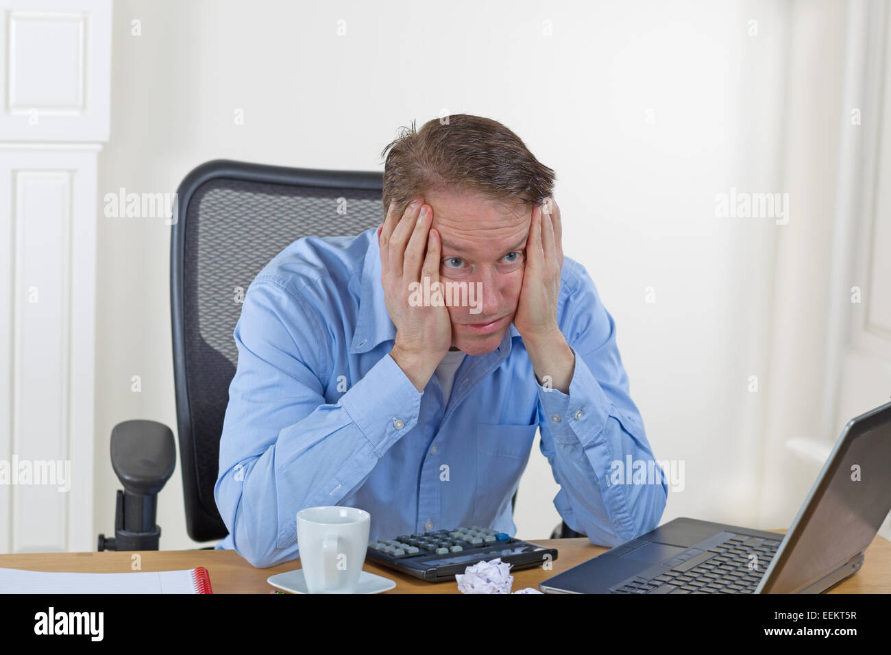 Reifer Mann mit Kopf in den Händen während der Suche mit Laptop, Rechner, gebrochene Stifte, wattierte Papier, Kaffeetasse und keine verloren Stockfoto