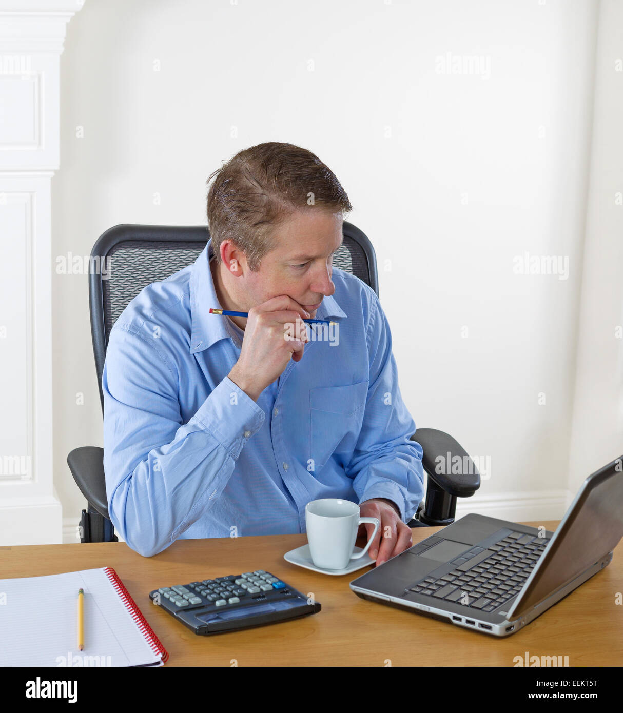 Reifen Mann Laptop-Bildschirm betrachten, Bleistift in der hand, während der Arbeit mit weißen Wand im Hintergrund Stockfoto
