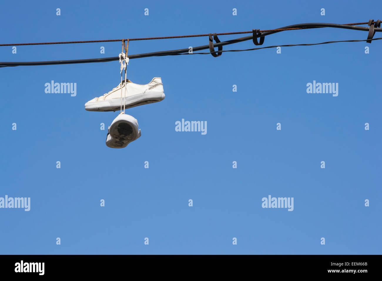 Sportschuhe, die in der Luft hängen, nachdem er über die Telefonleitungen auf blauen Himmelshintergrund geworfen Stockfoto
