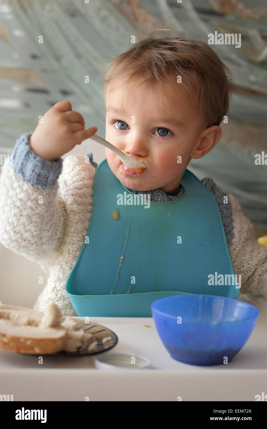 Porträt von Baby Boy (18-23 Monate) tragen Baby Lätzchen Essen am Tisch Stockfoto