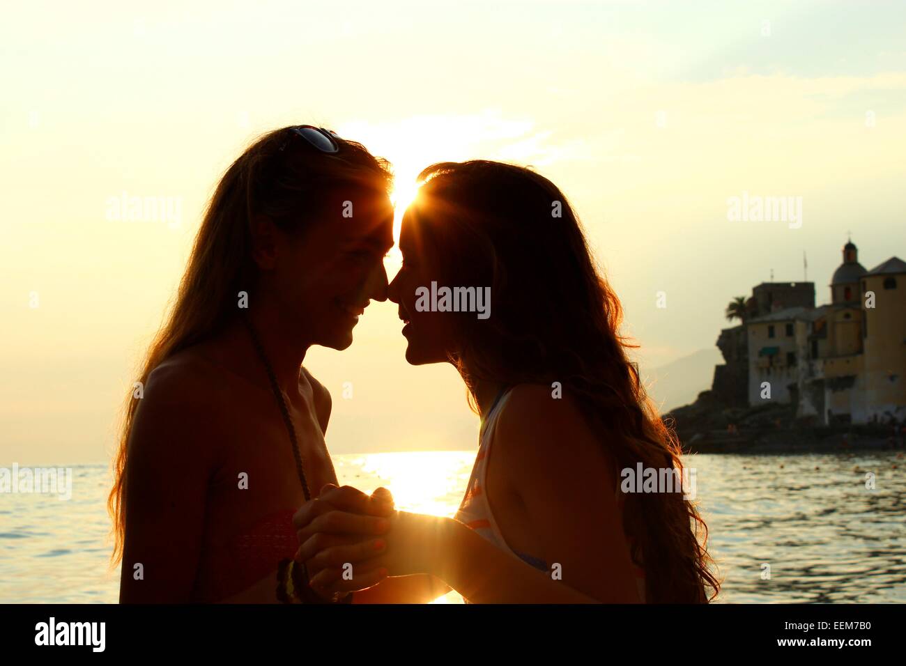 Junge Frauen, die Hand in Hand gegen Meer bei Sonnenuntergang Stockfoto