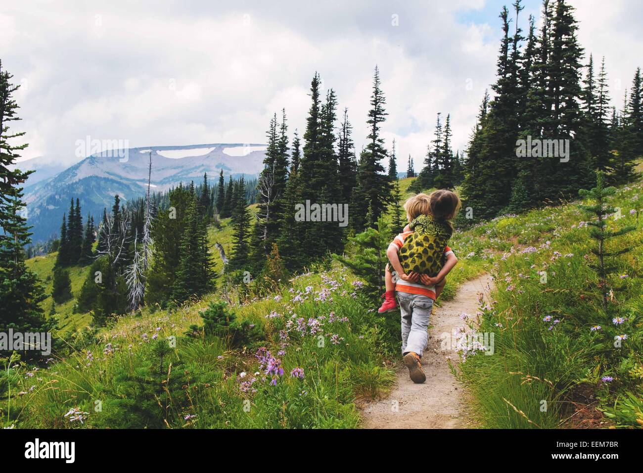 Junge, der auf einem Bergpfad entlang geht und seiner Schwester einen Huckepack-Ausflug in die USA gibt Stockfoto