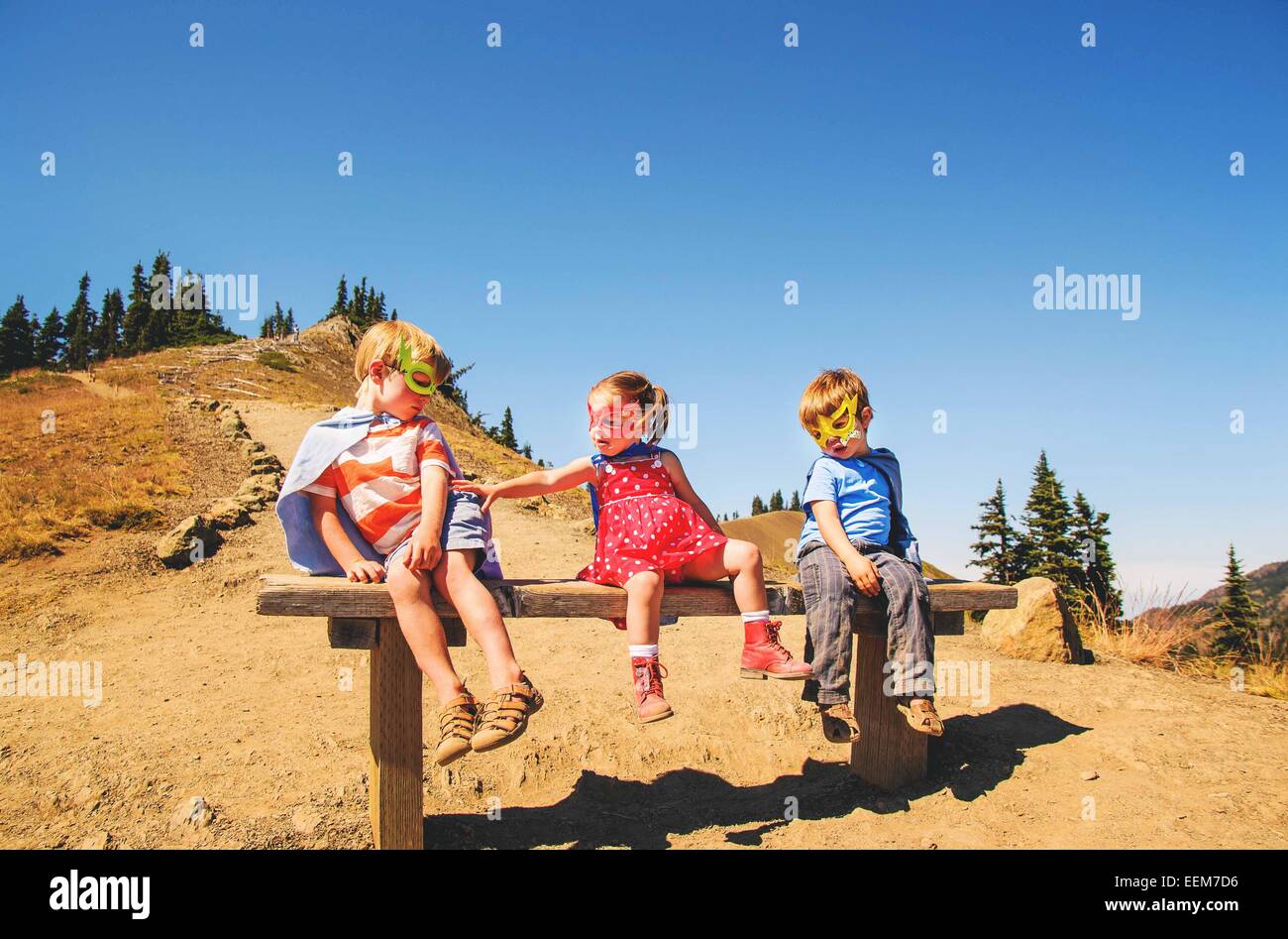 Drei Kinder, die als Superhelden verkleidet auf einer Bank sitzen Stockfoto