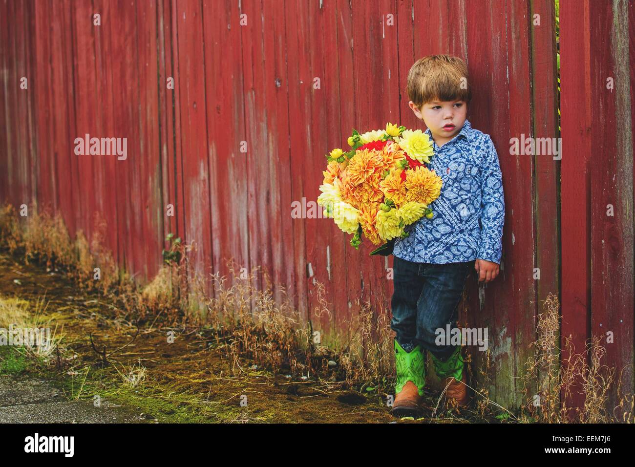 Junge, der an einer roten Wand steht und einen Blumenstrauß hält Stockfoto