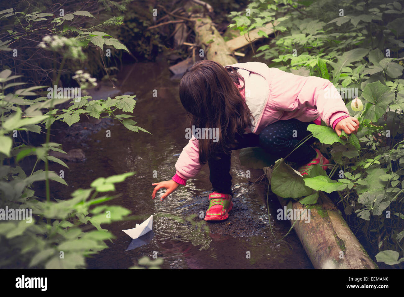 Kaukasische Mädchen schwimmende Papierschiff auf Forest creek Stockfoto