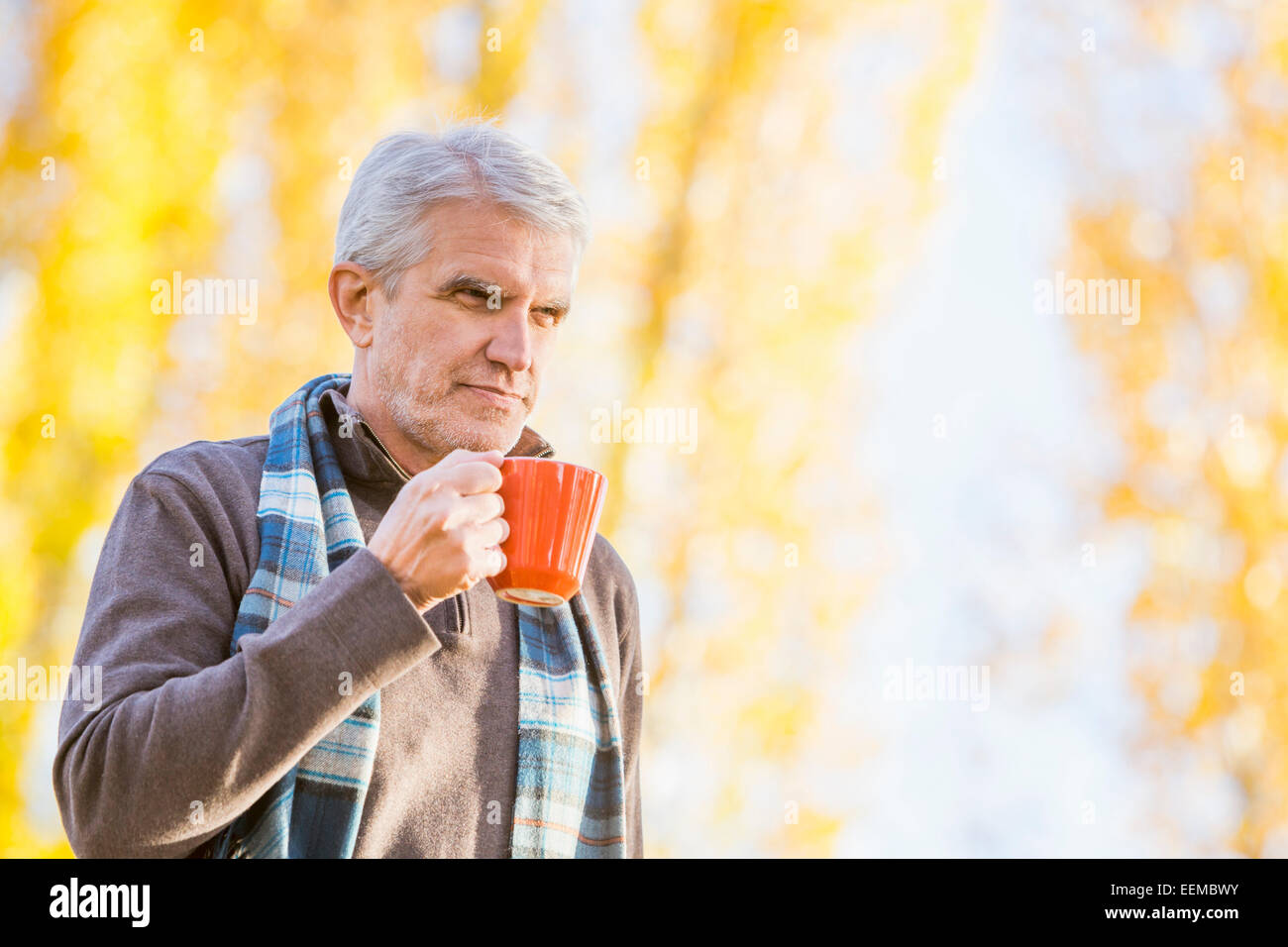 Älteren kaukasischen Mann Kaffeetrinken in der Nähe von Herbst Bäume Stockfoto