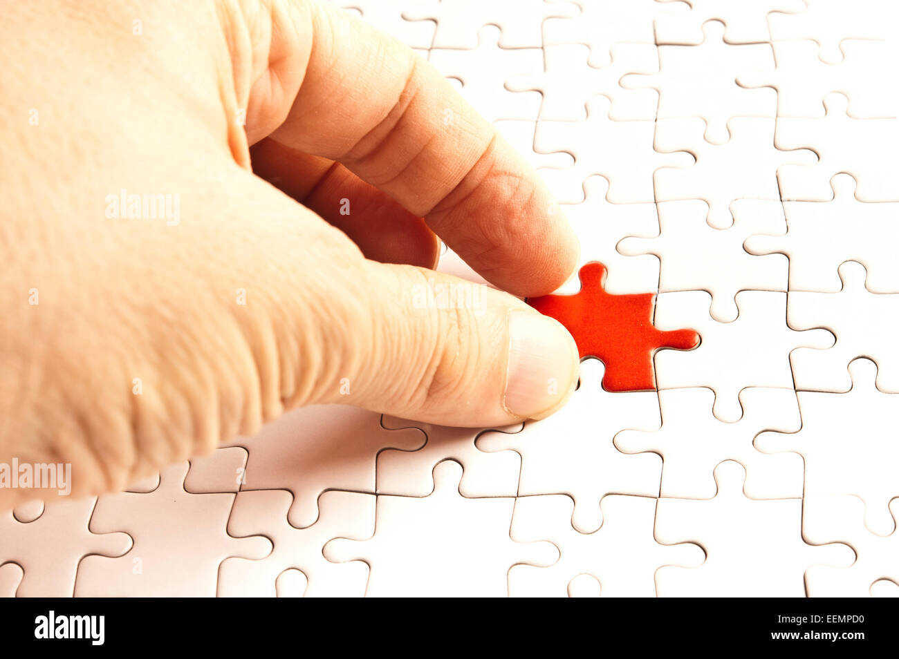 Hand des Menschen passend eine rote Puzzleteil um eine weiße Puzzle zu vervollständigen Stockfoto