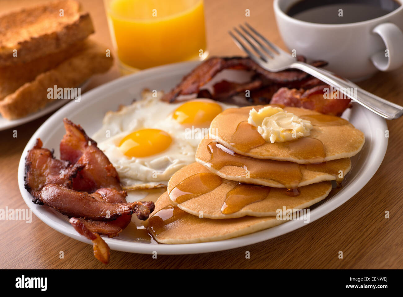 Ein leckeres Hauptart Frühstück mit knusprigem Speck, Eiern, Pfannkuchen, Toast, Kaffee und Orangensaft. Stockfoto