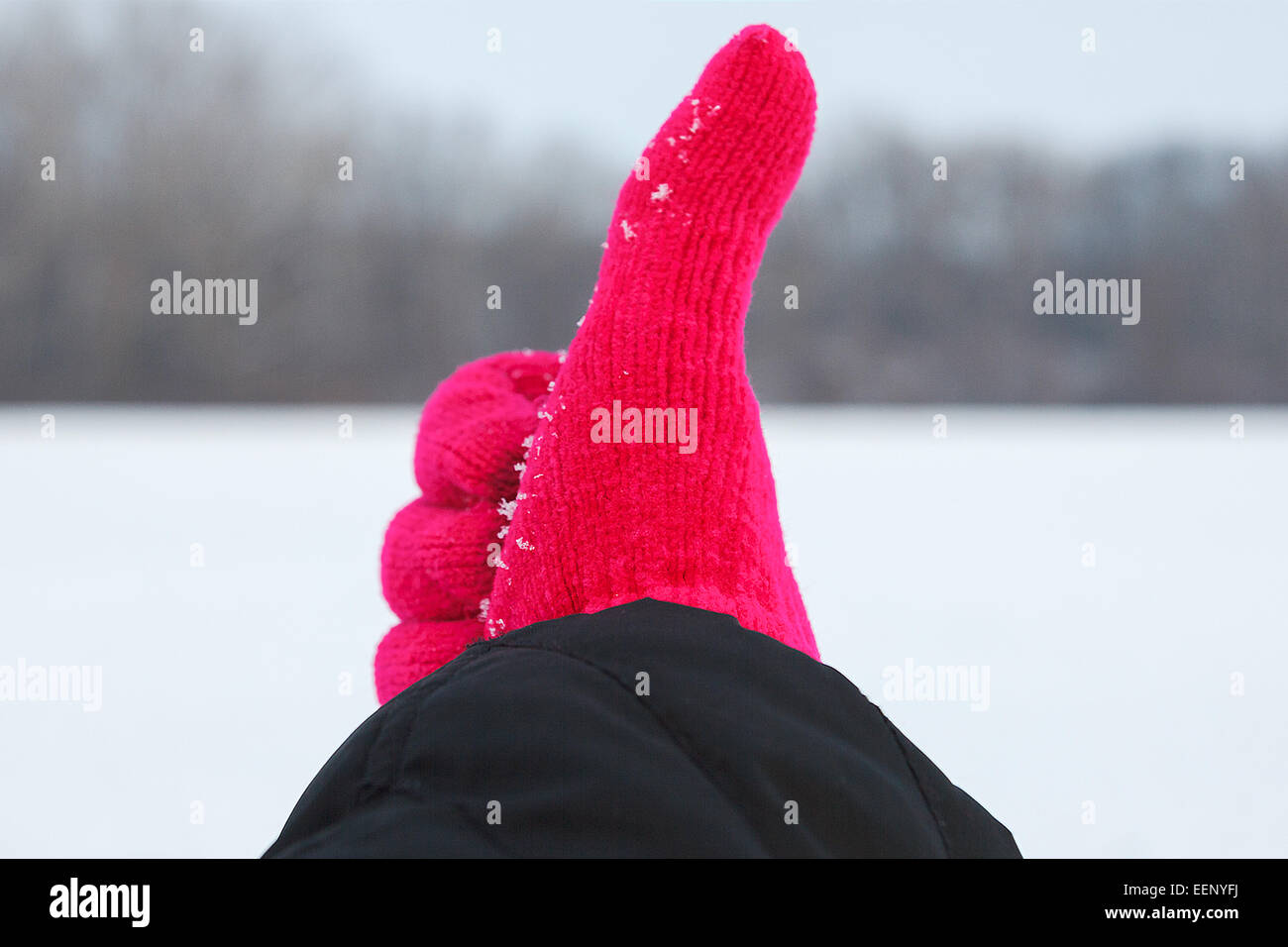 Foto von Hand in rot wollenen Handschuh mit Daumen oben auf Winter Hintergrund in der Natur, Konzept der Freude im winter Stockfoto