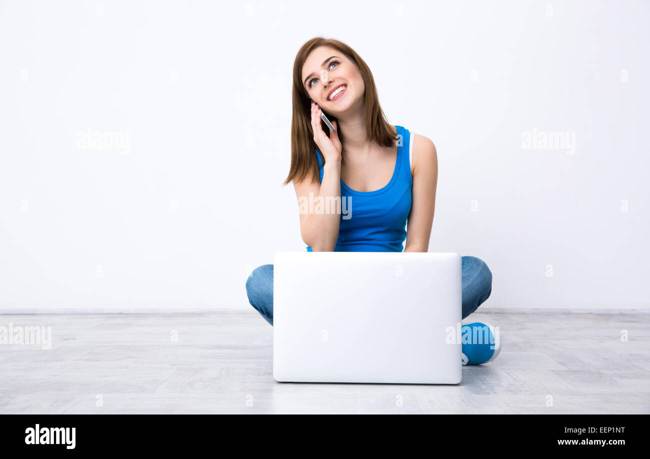 Glückliche Frau sitzen auf dem Boden mit Laptop und Telefon im Gespräch Stockfoto