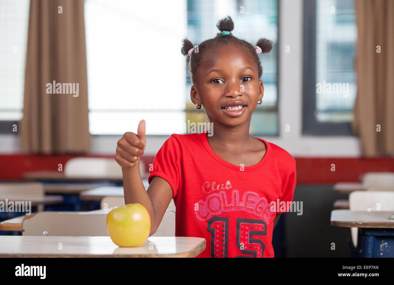 Junge Afro amerikanische schwarze Mädchen Klassenzimmer Rezeption lächelnd mit einem grünen Apfel. Stockfoto