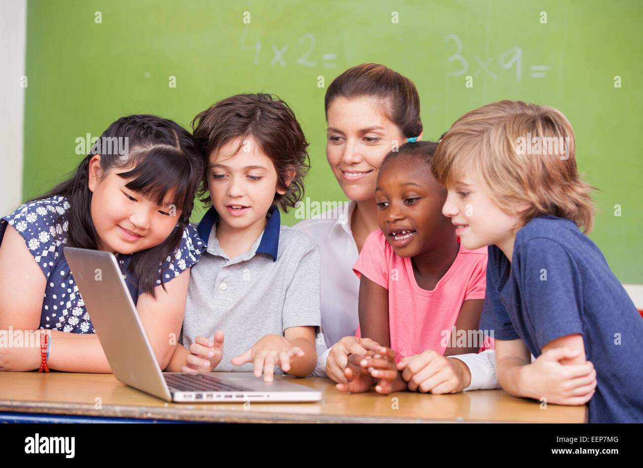 Interracial primäre Klassenzimmer lernen, Laptop mit ihrem Lehrer zu nutzen. Stockfoto