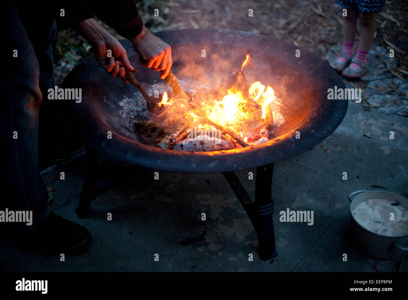 Ein Mann schürt die Kohlen eine Hinterhof-Feuerstelle. Stockfoto