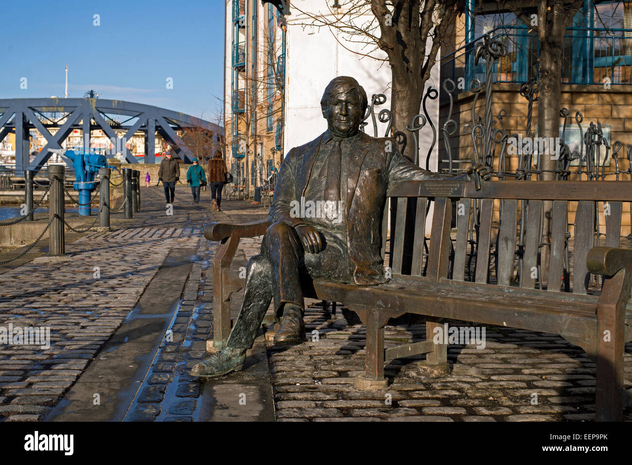 Lebensgroße Bronzeskulptur von Sandy Irvine Robertson OBE (1942 – 1999), sitzen auf einer Bank am Ufer, Leith, Edinburgh. Stockfoto