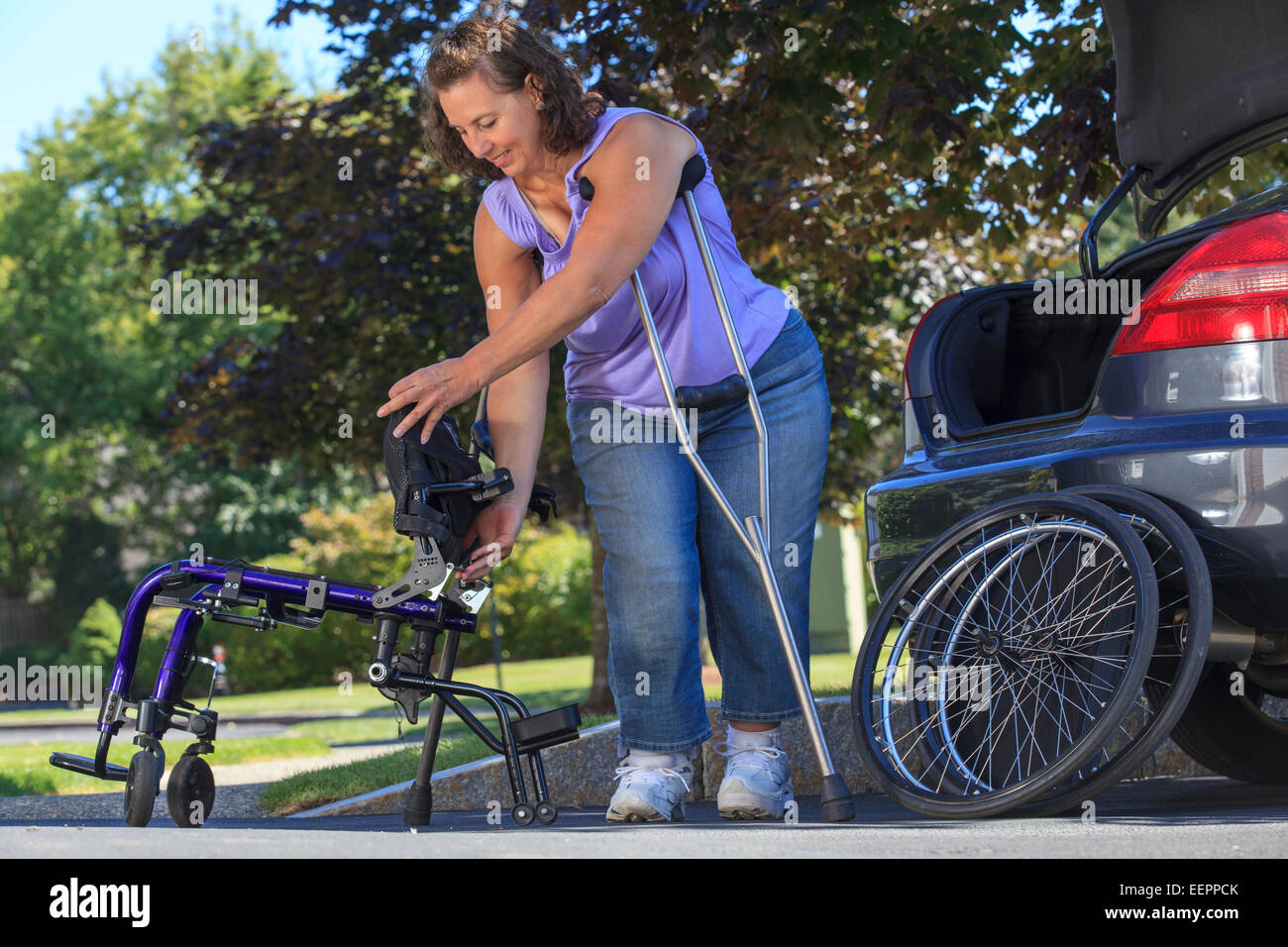 Frau mit Spina Bifida mit Krücken, um Rollstuhl auseinander zu nehmen, für die Reise im Auto Stockfoto