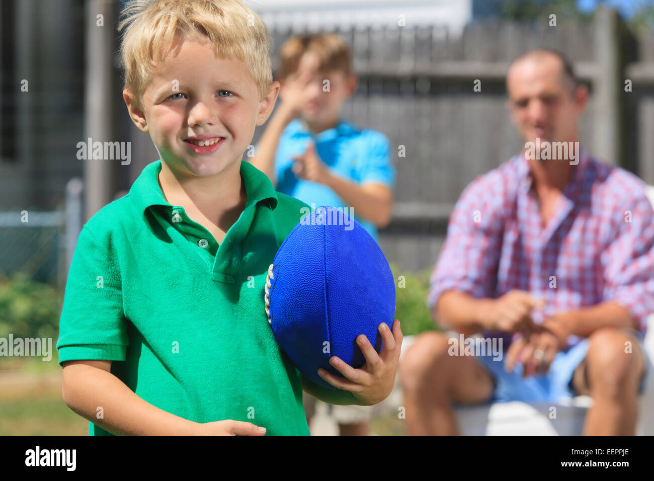 Fröhlicher Junge mit Vater und Bruder mit Hörschädigungen im Garten Fußball spielen Stockfoto