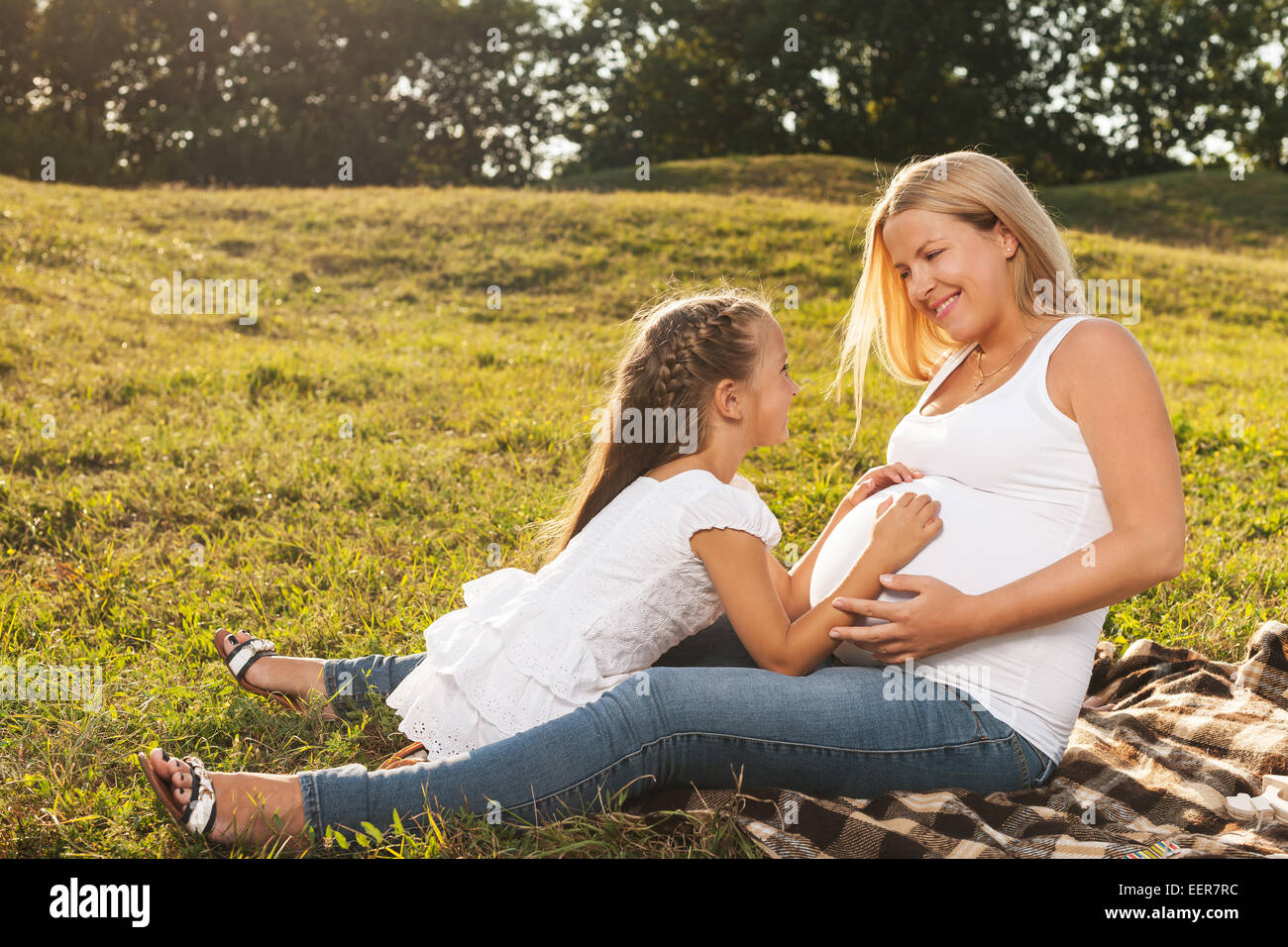 Niedliche kleine Mädchen umarmt ihre Mutter schwangeren Bauch. Glückliche Schwester freut sich über neue Baby treffen. Muttertag-Konzept Stockfoto