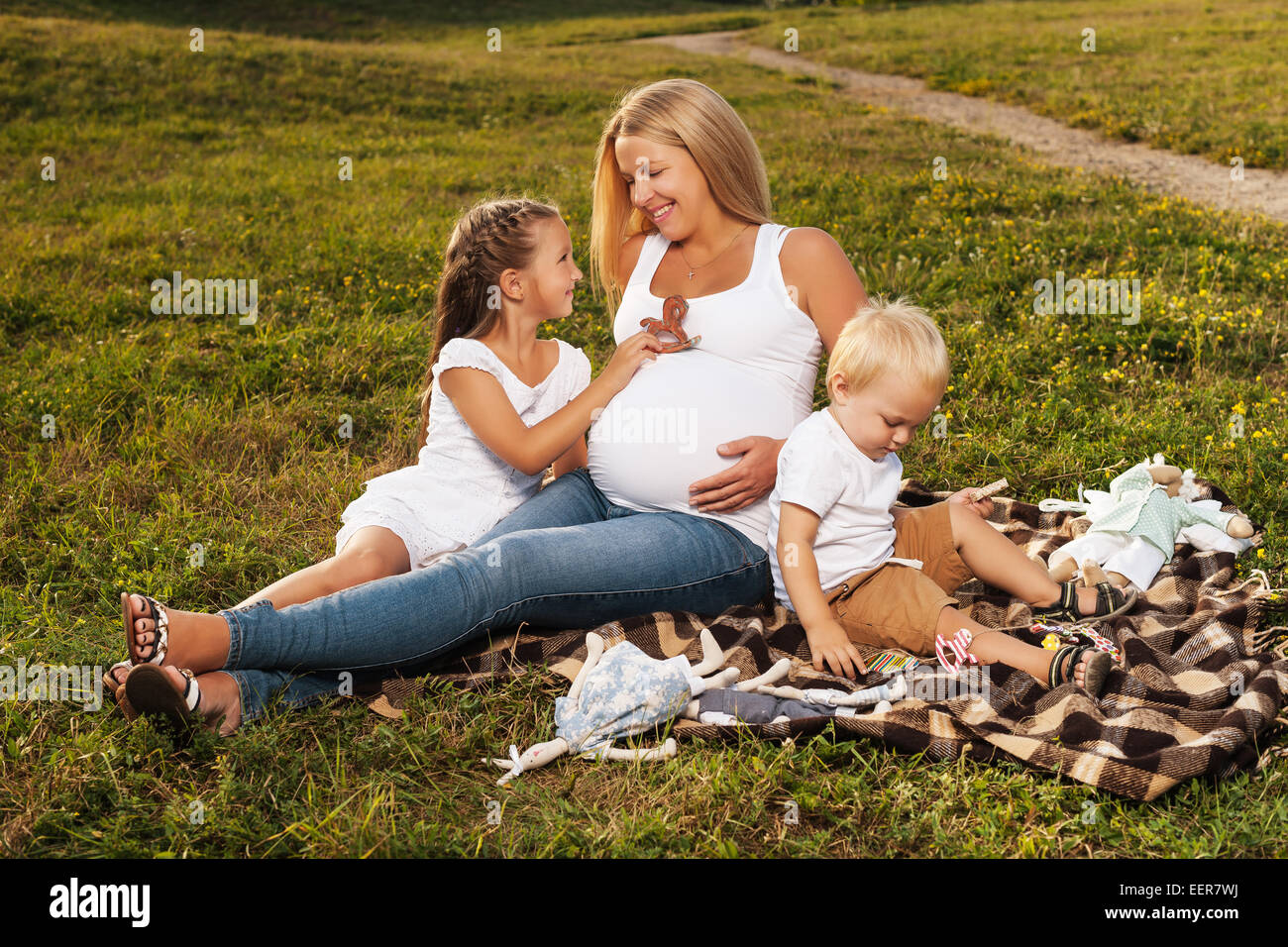 Schöne blonde schwangere Frau genießen ihre älteren Kinder-Gesellschaft. Mutter mit Kindern im Freien bei Sonnenlicht. Muttertag-Konzept Stockfoto