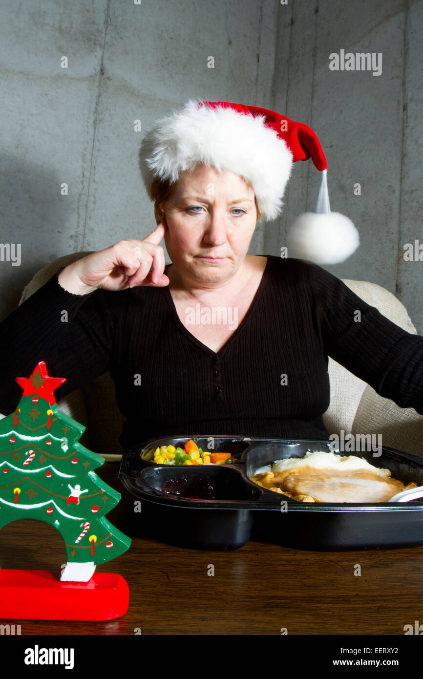 Unglückliche Frau, die einen Weihnachts-Strumpf-Hut Essen eine Türkei TV Dinner auf einem Tablett-Tisch im Keller Stockfoto