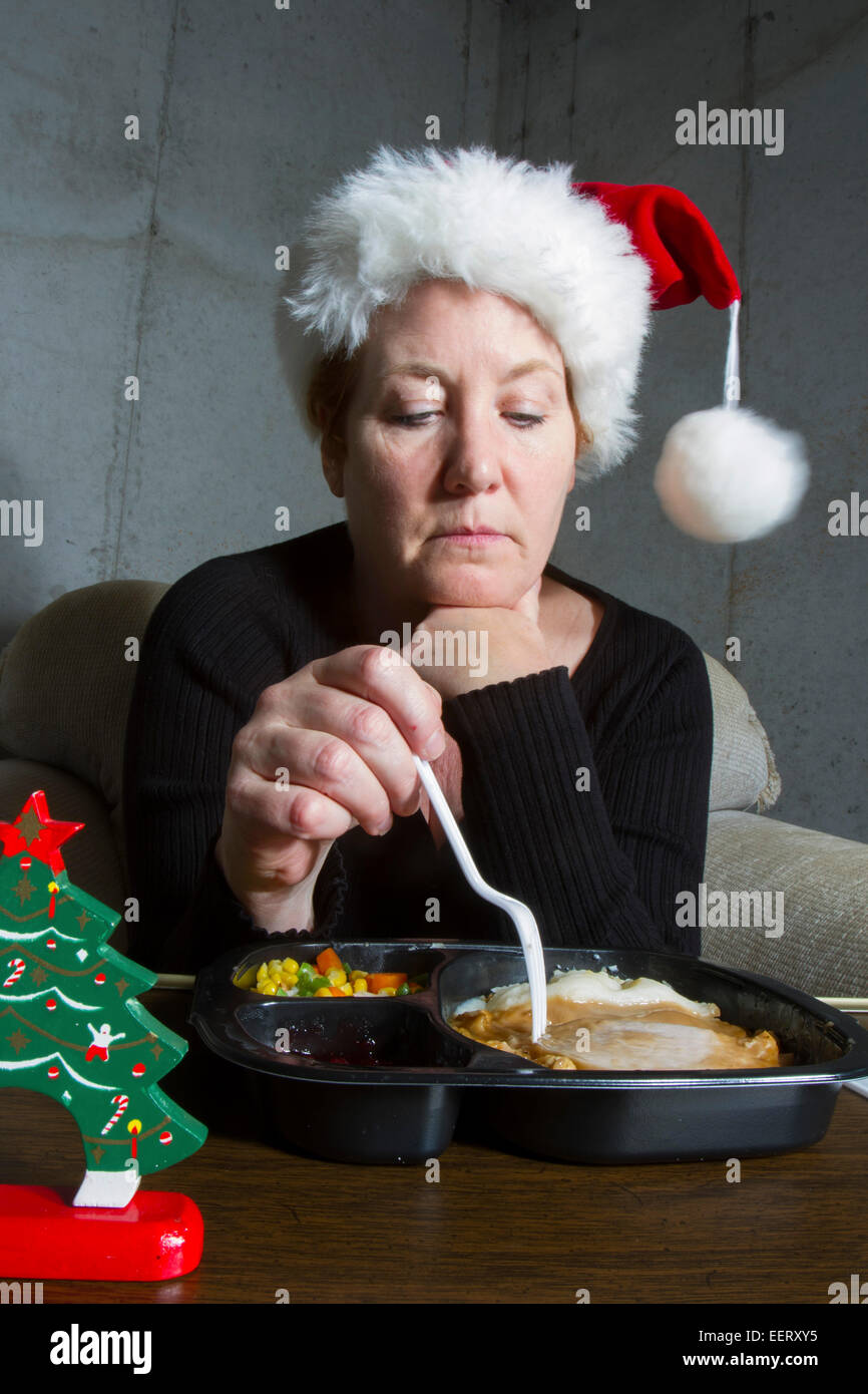 Unglückliche Frau, die einen Weihnachts-Strumpf-Hut Essen eine Türkei TV Dinner auf einem Tablett-Tisch im Keller Stockfoto