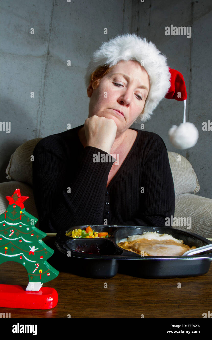 Unglückliche Frau, die einen Weihnachts-Strumpf-Hut Essen eine Türkei TV Dinner auf einem Tablett-Tisch im Keller Stockfoto