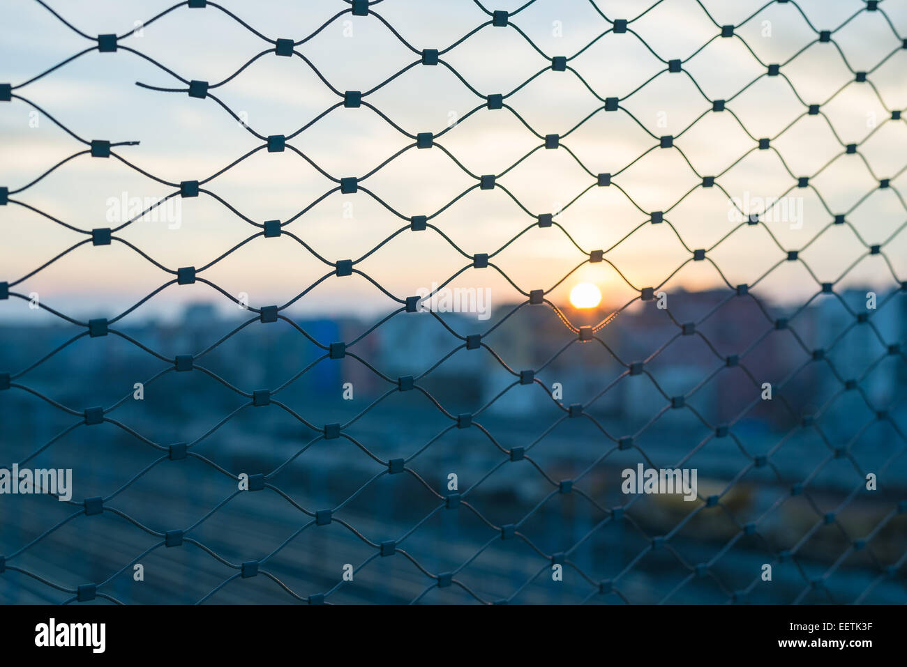 Selektiven Fokus auf Metallzaun bei Gegenlicht bei Sonnenuntergang. Verschwommene allgemeine Stadtbild im Hintergrund. Konzept der Überfüllung. Stockfoto