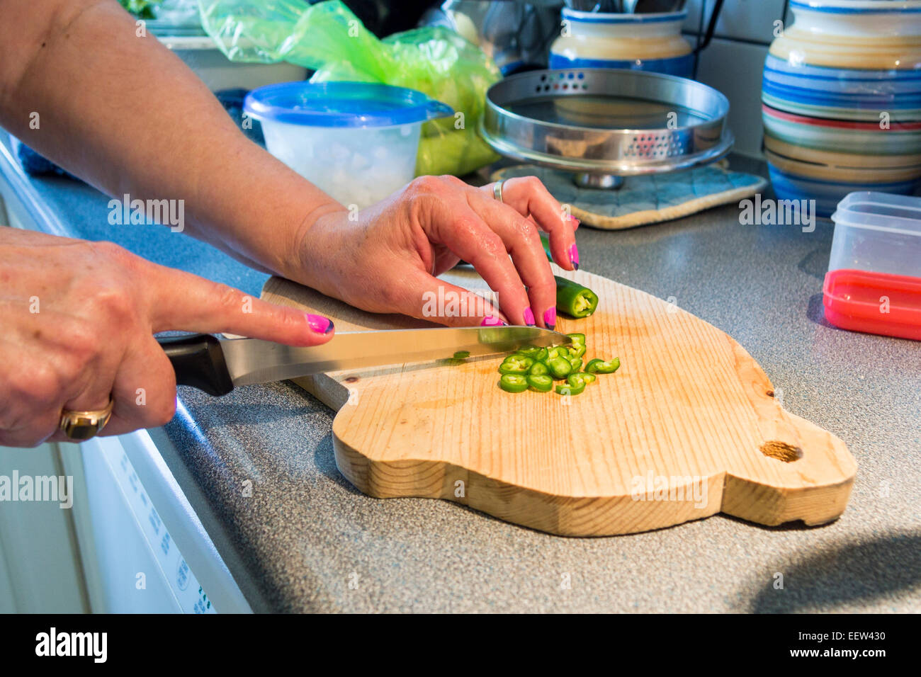 Precision Cuts Jalapeño Pfeffer. Eine Frau mit neu lackierte Fingernägel schneidet Jalapeño Paprika in sehr kleine Stücke Stockfoto