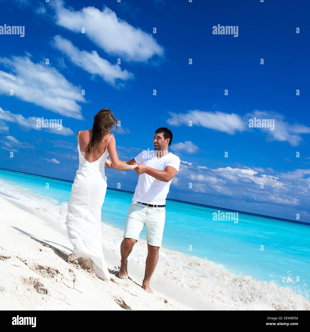 Glückliche Brautpaar in weißen Kleidern, die Spaß am Strand mit türkisfarbenem Meer Hintergrund Stockfoto