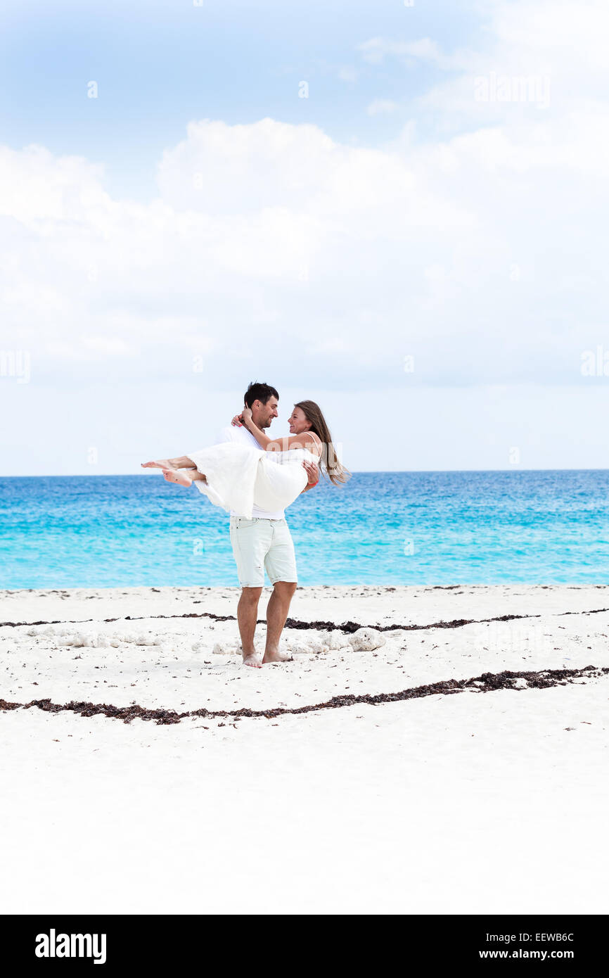 Glückliche Brautpaar in weißen Kleidern, die Spaß am Strand mit türkisfarbenem Meer Hintergrund Stockfoto