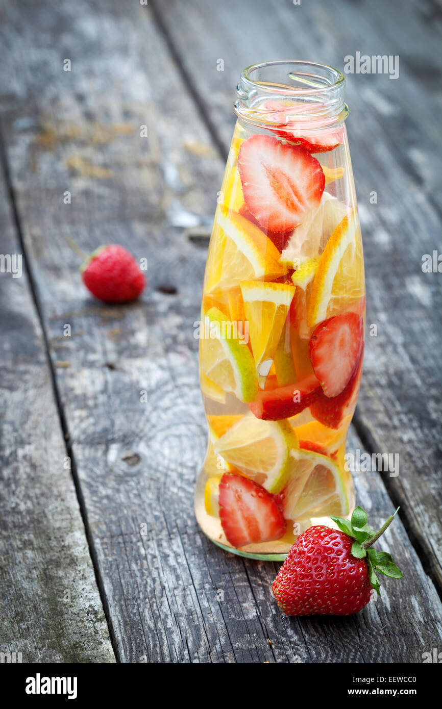 Flasche mit in Scheiben geschnittenen Orangen und Erdbeeren auf Holztisch, Bio Vegan Getränk Stockfoto