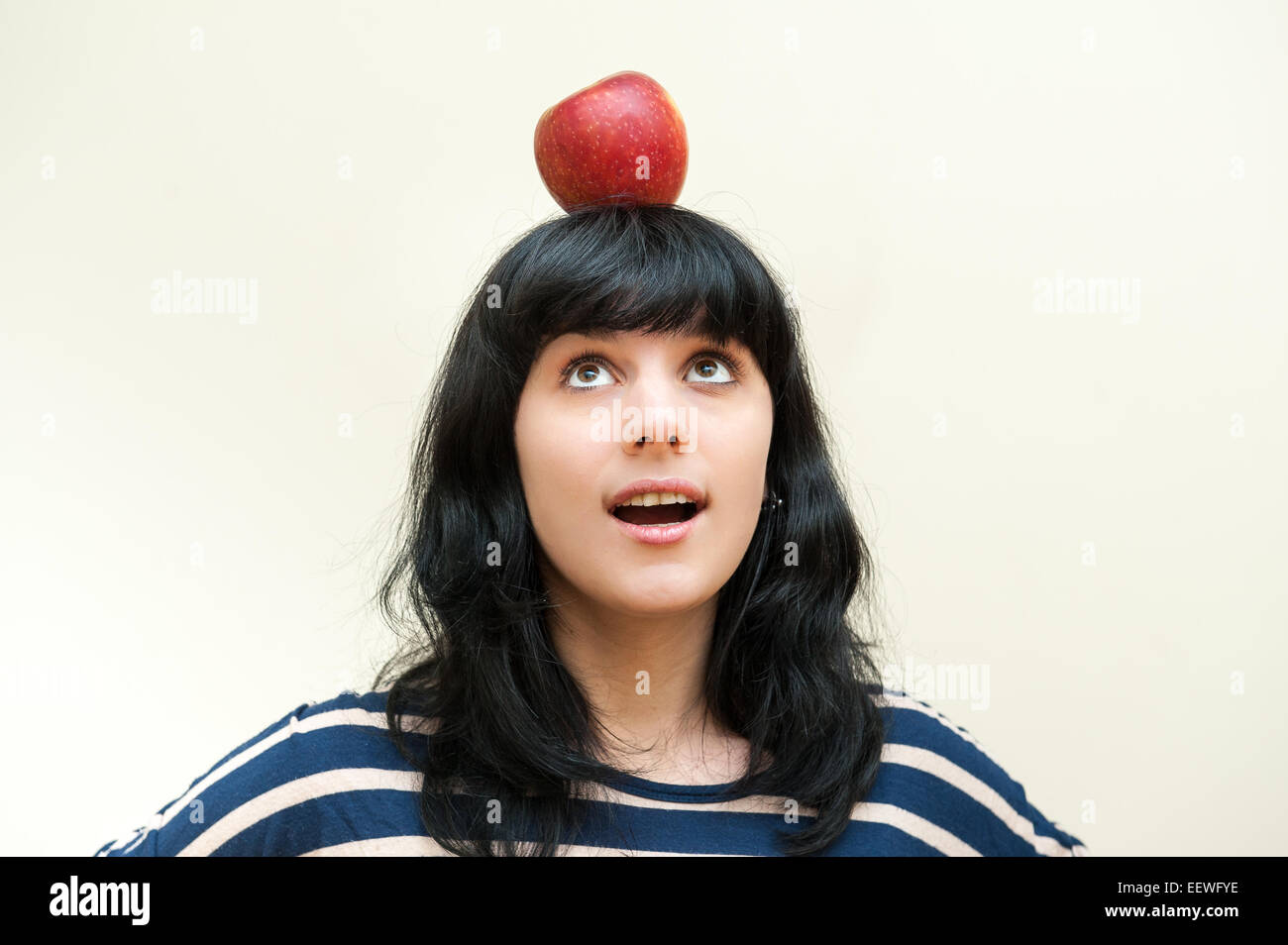 Hübsche Brünette Mädchen Lächeln auf den Lippen und auf der Suche nach roter Apfel auf dem Kopf auf weißem Hintergrund Stockfoto