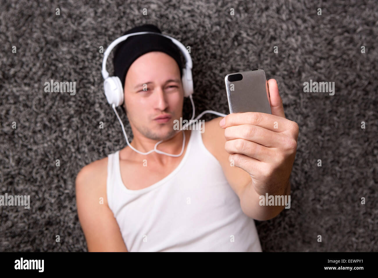 Attraktiver Mann mit Kopfhörern in einem weißen Hemd macht Selfie mit seinem Handy Stockfoto