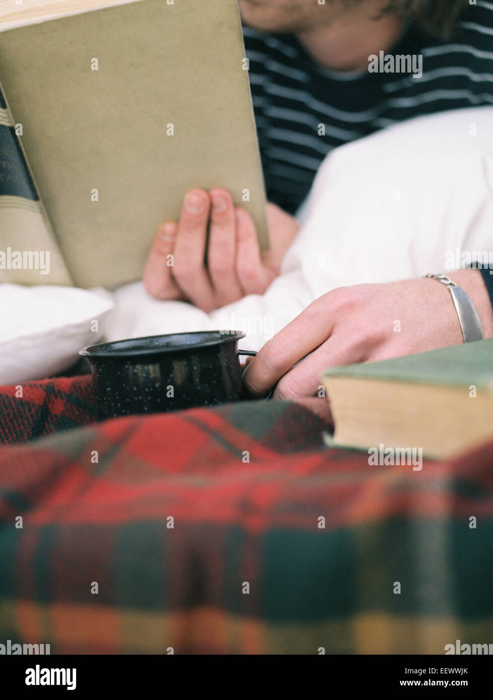 Der junge Mann ein Buch lesen, hält einen Becher hautnah. Stockfoto