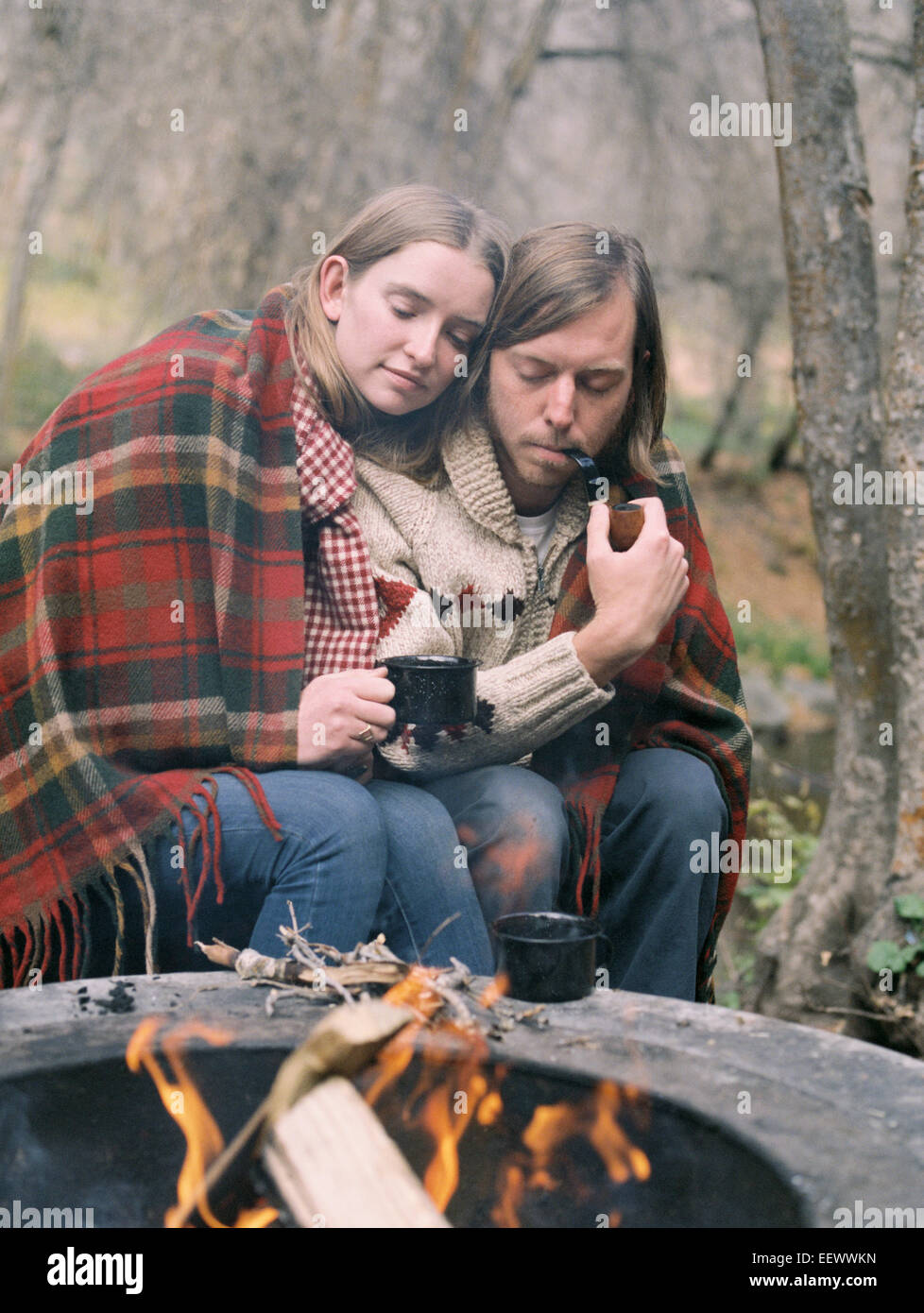 Junges Paar sitzt an einer Feuerstelle, in eine Decke gehüllt. Stockfoto
