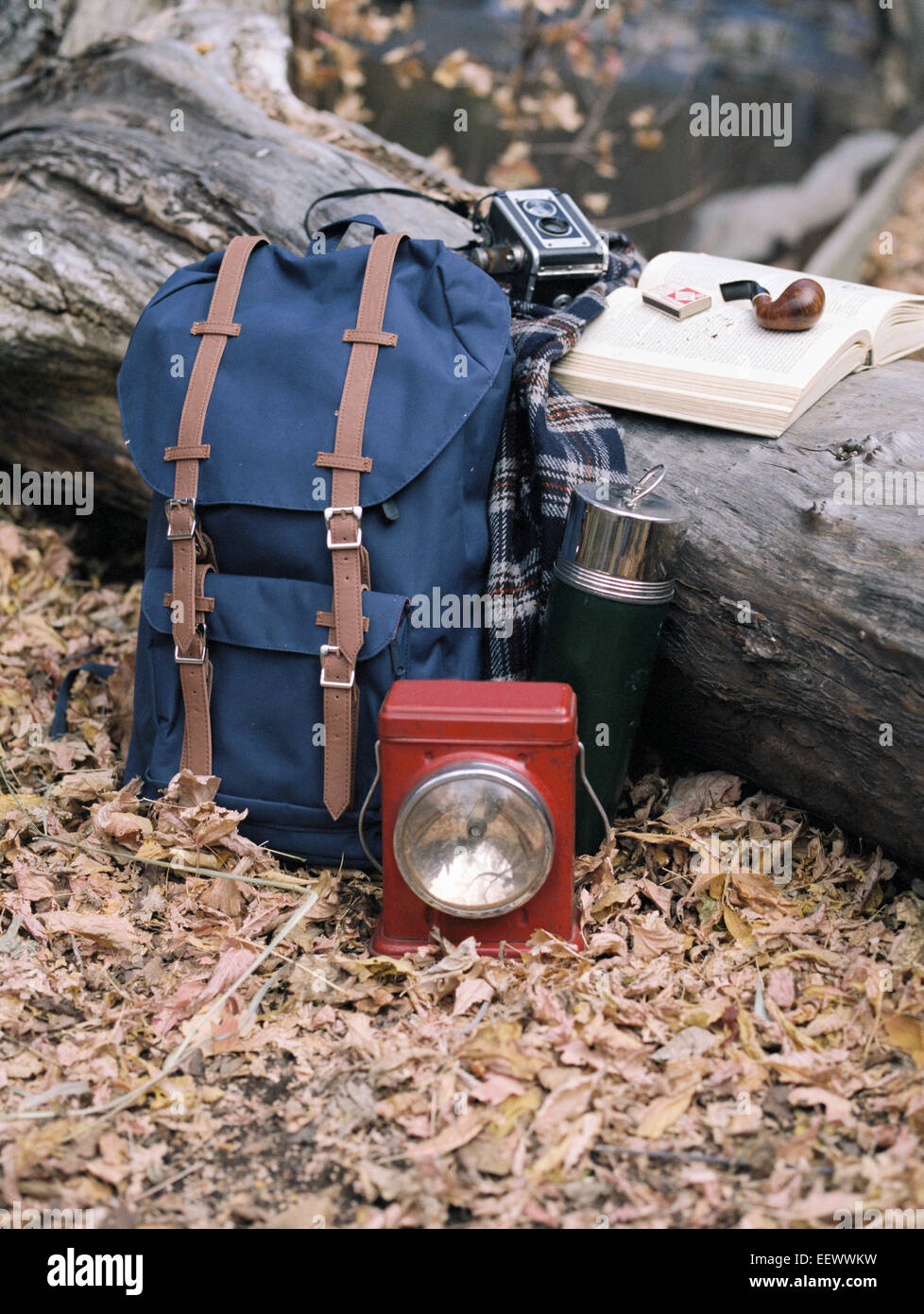 Wandern Ausrüstung, Rucksack, Taschenlampe, Kolben und Kamera durch einen Baumstamm. Ein Rohr auf ein offenes Buch liegen. Stockfoto